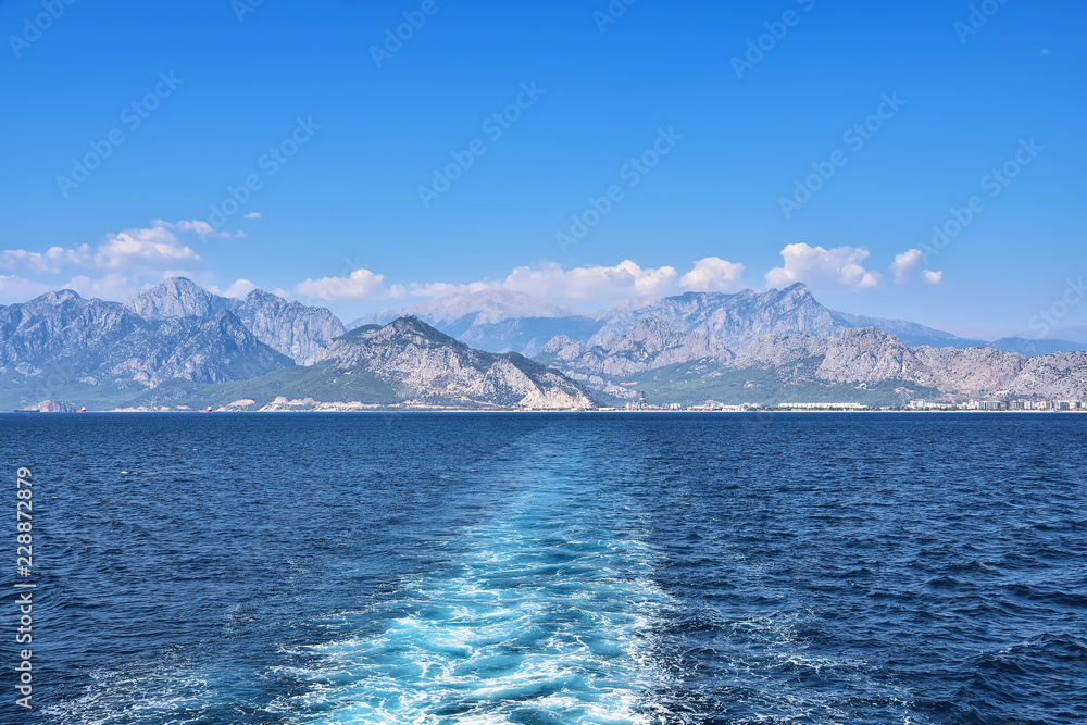 view from the sea on the coast of Antalya, in the background of the building, mountains, against the background of blue sky and clouds