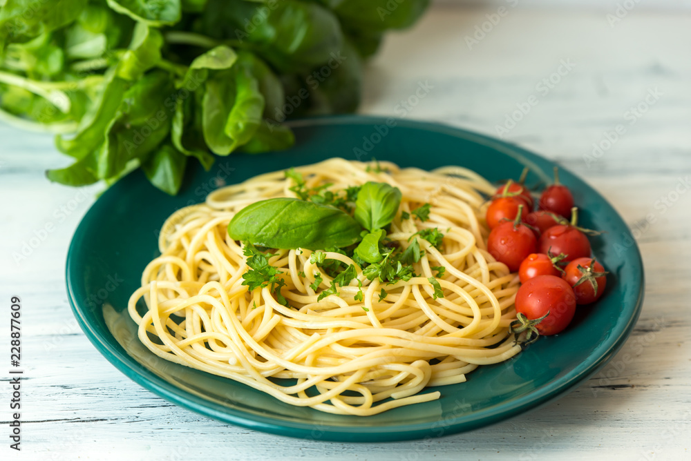 pasta with herbs, basil and tomato served on a green plate in a rustic kitchen