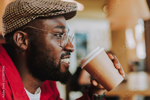 Cheerful relaxed bearded man looking into the distance and smiling while enjoying his delicious coffee