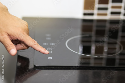 Hand switch on a modern black induction hob in a kitchen. 