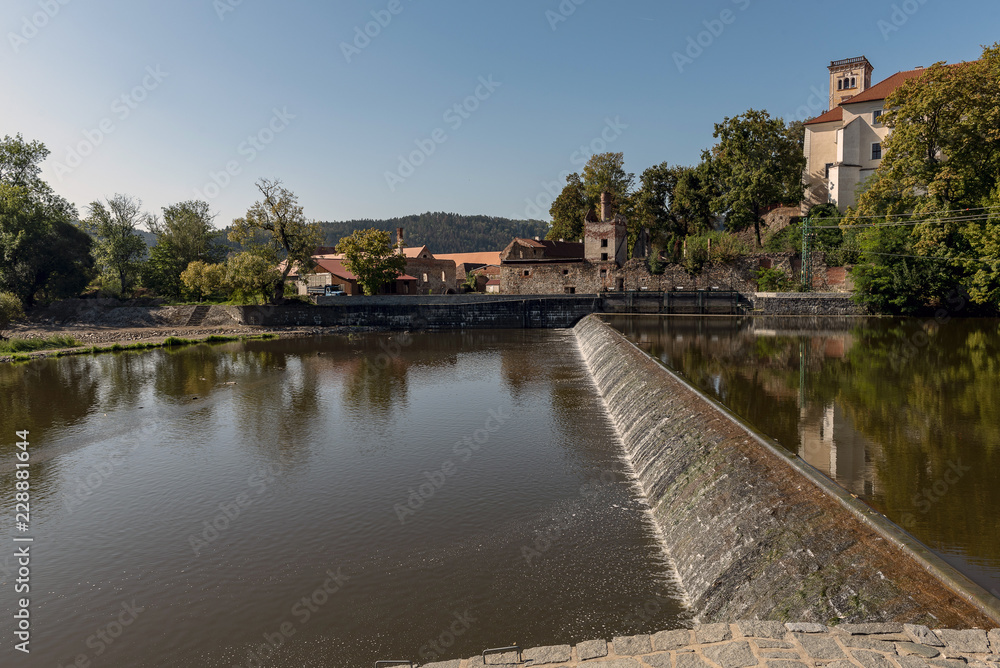sun-lit weirs on the river Sazava in the background of the Sázava monastery building