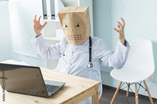 Healthcare, medical and people concept - online doctor wearing paper mask with sad face sitting at table with laptop photo