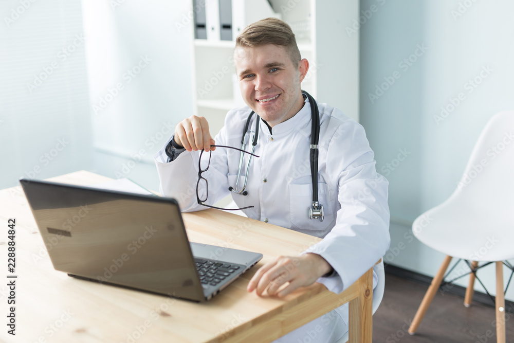 Medicine, working and people concept - doctor sitting at the table with laptop and smiling Medicine, working and people concept - doctor sitting at the table with laptop and smiling