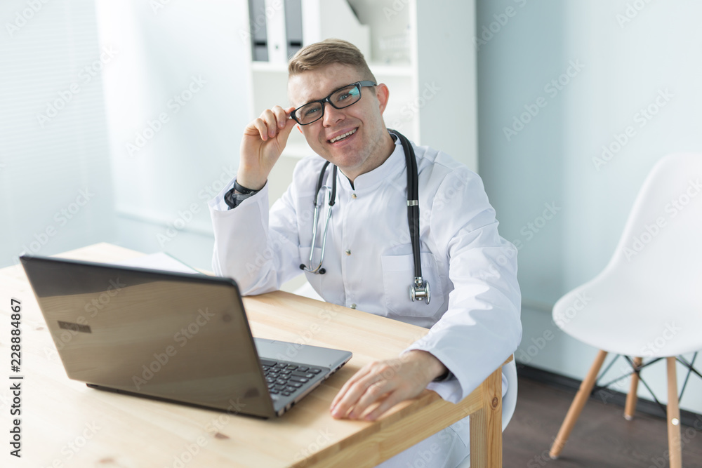 Healthcare, medical and people concept - Young caucasian doctor sitting in his office and smiling Healthcare, medical and people concept - Young caucasian doctor sitting in his office and smiling