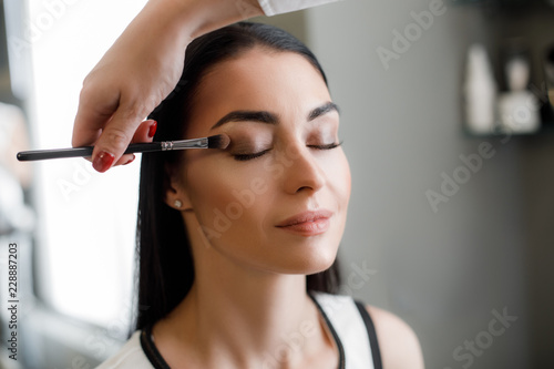 Makeup artist using eyeshadows of dark shades and applying them to corner of woman eye