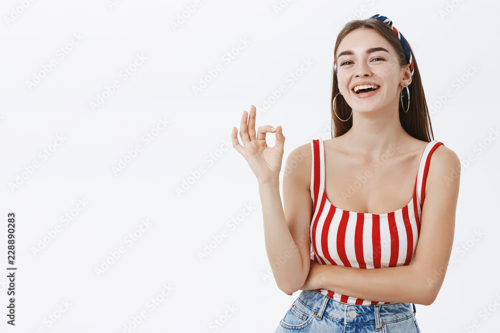 Carefree relaxed and joyful european pinup woman in headband and striped red top showing okay or excellent gesture approving outfit of friend laughing and smiling happily over grey wall Carefree relaxed and joyful european pinup woman in headband and striped red top showing okay or excellent gesture approving outfit of friend laughing and smiling happily over grey wall