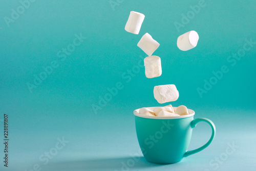 Marshmallow falling into cup over bright turquoise