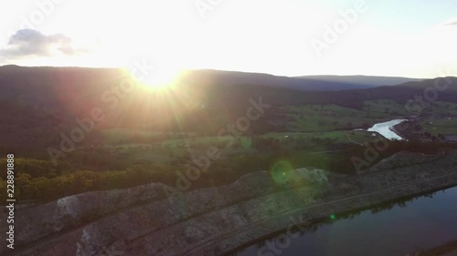 Cinematic aerial pan across beautiful countryside and mountains facing the sun with lens flare at sunset