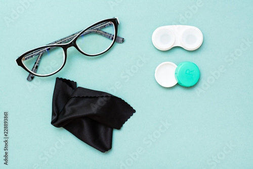 Open container with lenses, glasses and cleaning cloth on a green background. Top view. Copy space photo