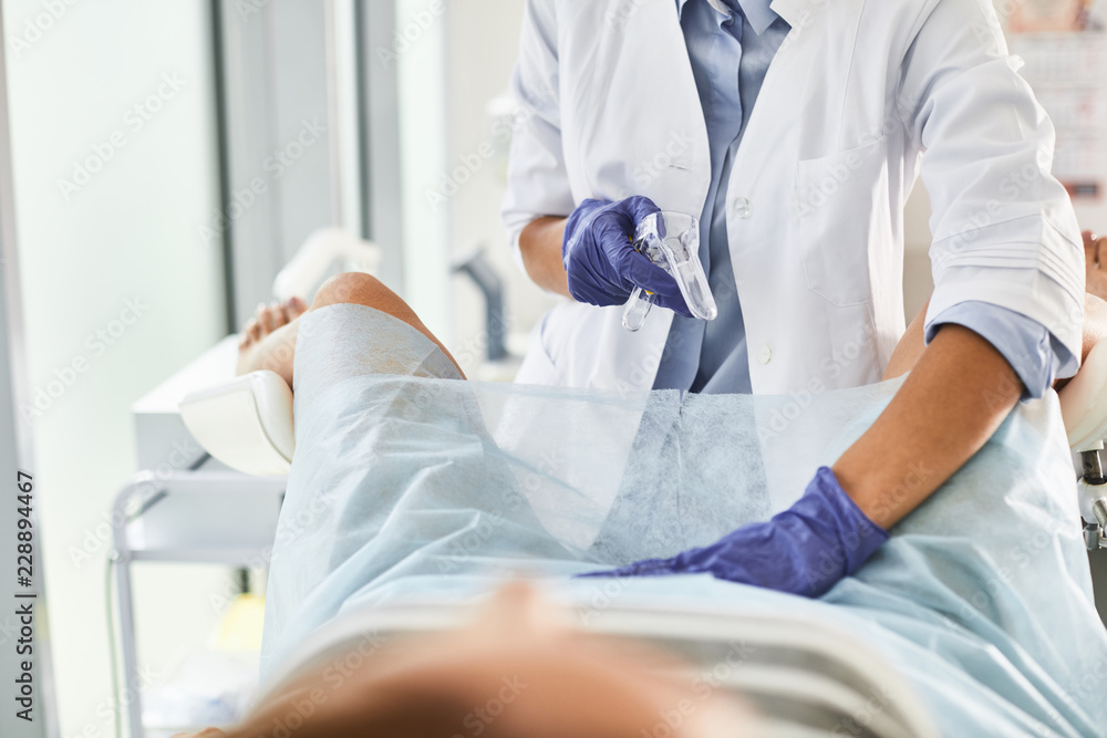 Cropped portrait of gynecologist in white lab coat and sterile gloves using vaginal speculum