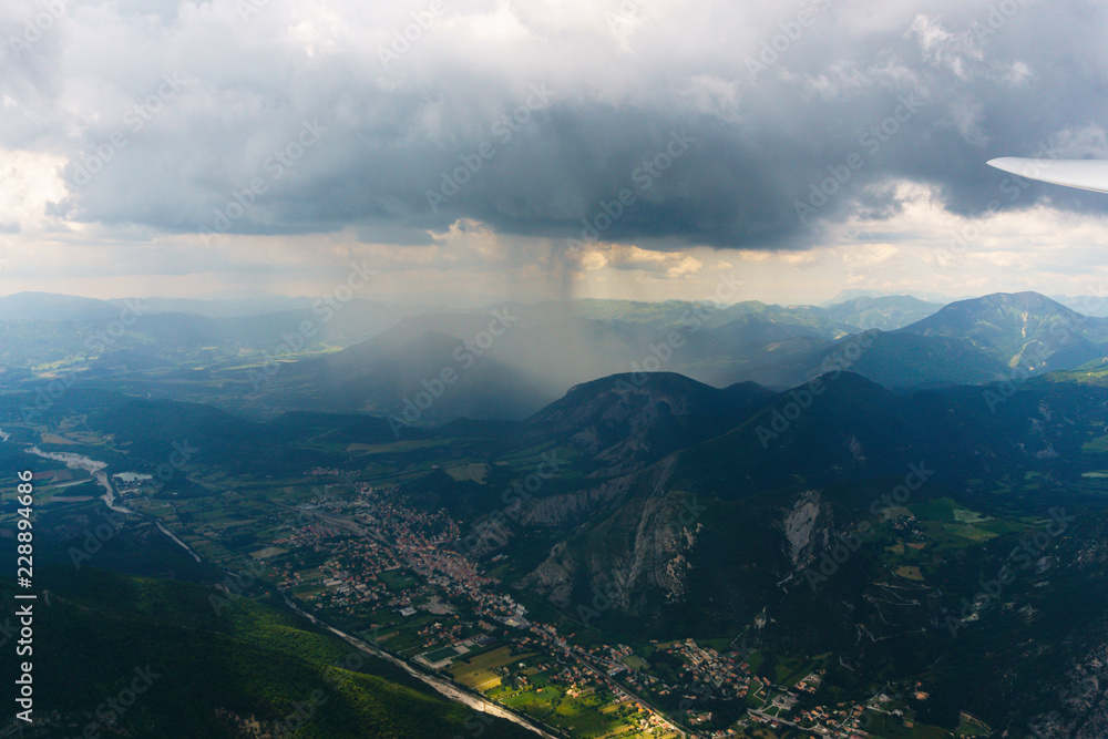 Obraz premium Luftaufnahme aus einem Segelflugzeug mit Blick über eine Berglandschaft im Regen
