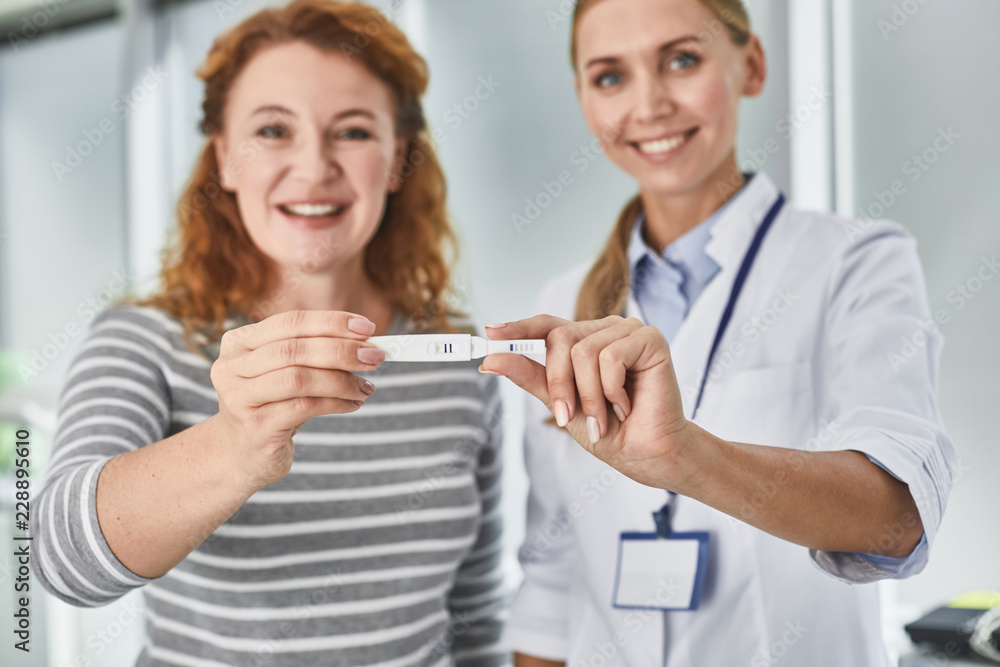 Portrait of joyful gynecologist and red-haired woman sharing happy news about future baby. They looking at camera and smiling Portrait of joyful gynecologist and red-haired woman sharing happy news about future baby. They looking at camera and smiling