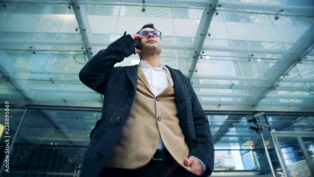 An entrepreneur is having a serious phonecall in the middle of a business complex. Red epic cinema camera footage. An entrepreneur is having a serious phonecall in the middle of a business complex. Red epic cinema camera footage.