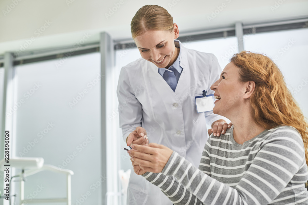 I am going to be a mom. Portrait of smiling young gynecologist standing near red-haired woman and looking at photo of her child I am going to be a mom. Portrait of smiling young gynecologist standing near red-haired woman and looking at photo of her child