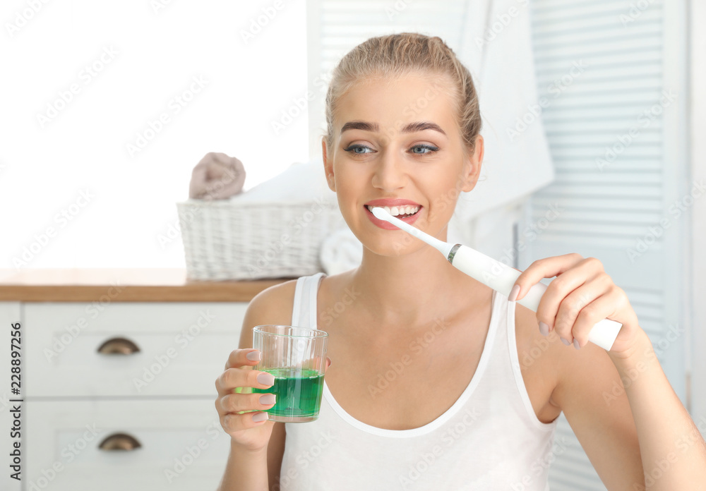Woman brushing teeth and holding glass with mouthwash in bathroom Woman brushing teeth and holding glass with mouthwash in bathroom