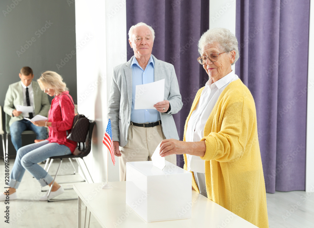Fototapeta premium Elderly woman putting ballot paper into box at polling station