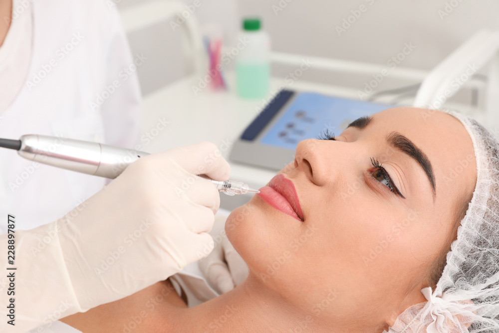 Obraz premium Młoda kobieta przechodzi procedurę permanentnego wargi makeup w tatuażu salonie, zbliżenie