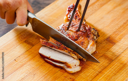 Chef hand with knife cutting meat on wooden board. photo