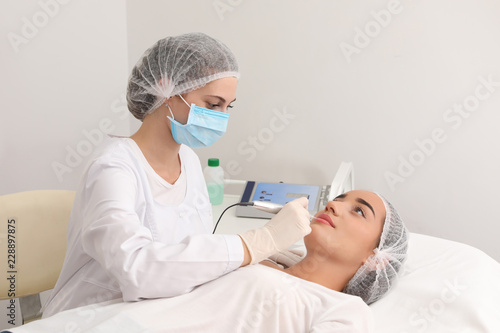 Young woman undergoing procedure of permanent lip makeup in tattoo salon