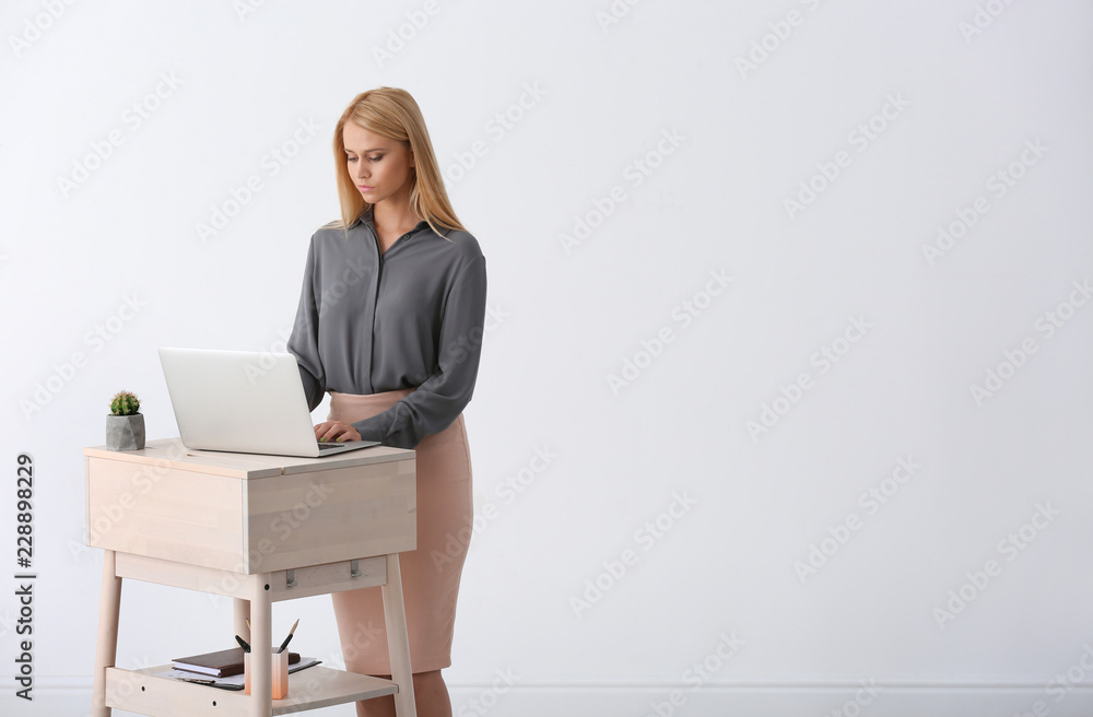 Young woman using laptop at stand up workplace against white wall. Space for text Young woman using laptop at stand up workplace against white wall. Space for text
