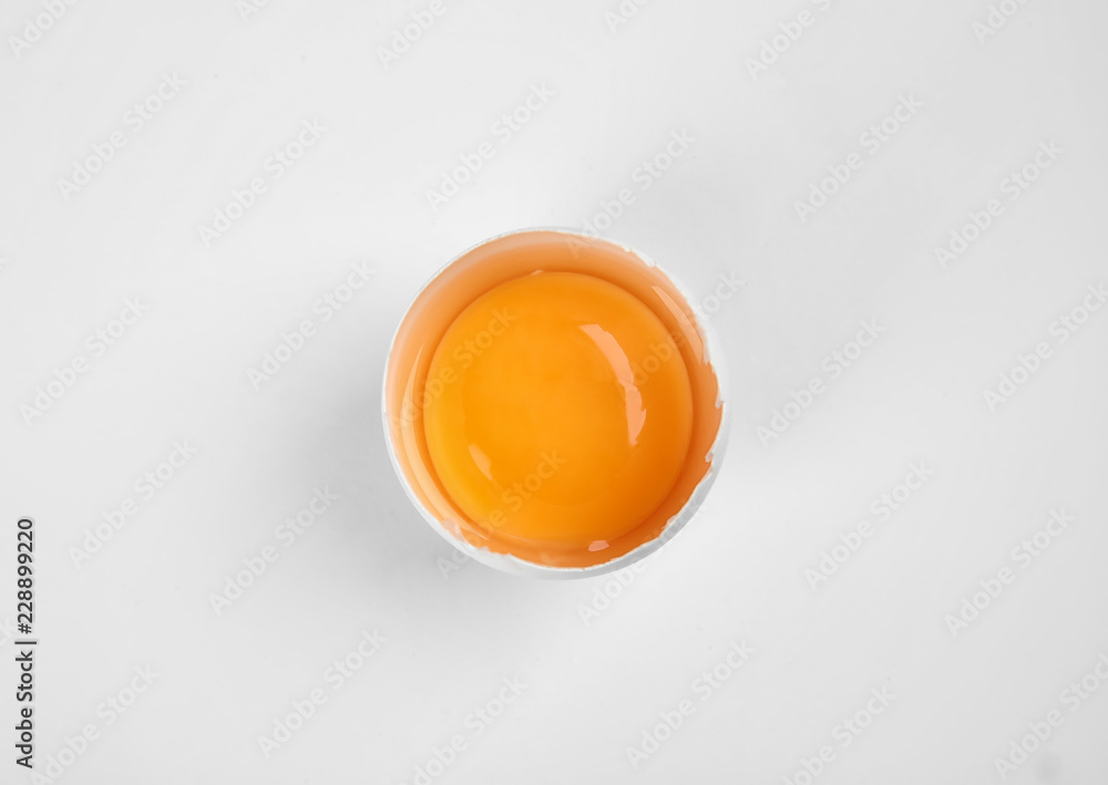 Cracked raw chicken egg with yolk on white background, top view
