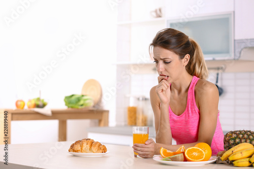 Woman choosing between dessert and fruits at table in kitchen. Healthy diet
