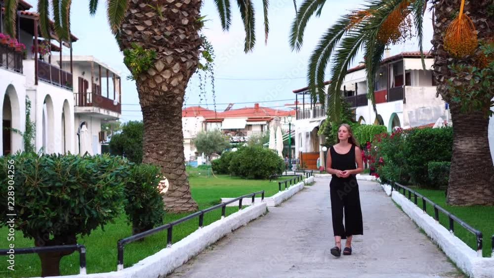 Young attractive dreamy woman in black casual clothes having evening walk in tropical plant garden on palm tree resort Young attractive dreamy woman in black casual clothes having evening walk in tropical plant garden on palm tree resort