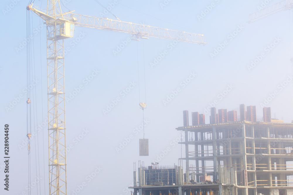Tower cranes on the construction of a building with a frame of reinforced concrete. Works in the morning mist.