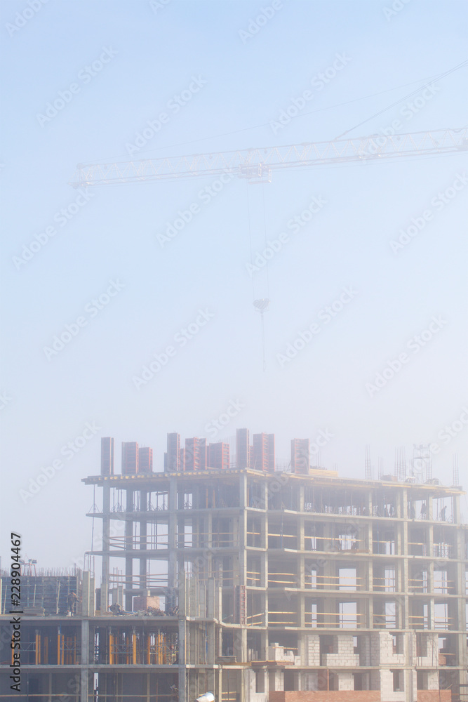 Tower cranes on the construction of a building with a frame of reinforced concrete. Works in the morning mist.