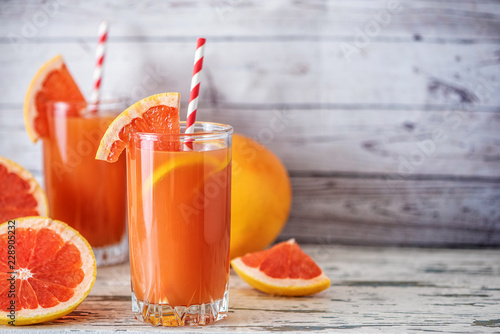 Fresh grapefruits and two glasses of grapefruit juice on light wooden table. With copy space