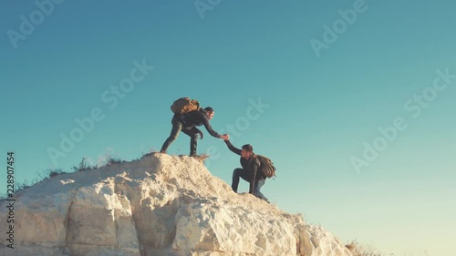 Climber helping teammate climb, the man with the backpack reached out a helping hand to his friend. Hiker helping friend while trekking on hill. Tourist man helps someone to climb the mountain.