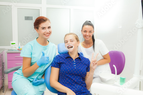 Young women dentist, assistant, patient in the treatment room looking at the camera. Patient with expander and braces
