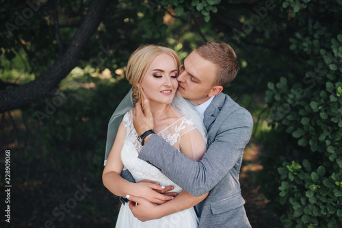 Beautiful newlyweds hugging and smiling cute in a park with green trees. Wedding portrait of a cheerful bride and gentle bride. Wedding photography.