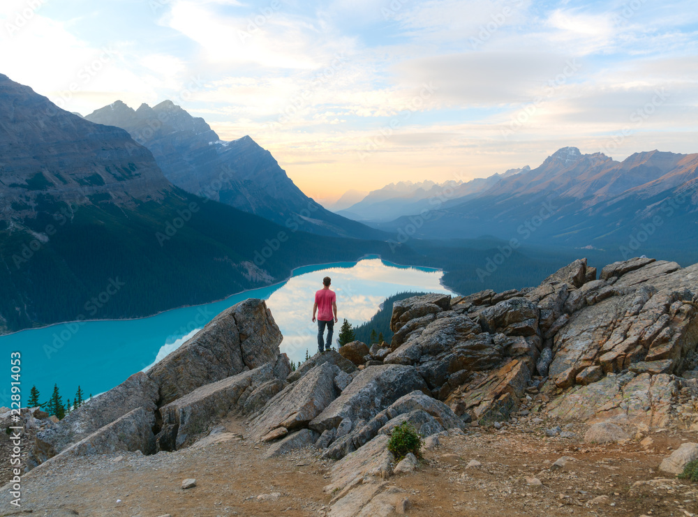 A lone figure watches the sun set over Peyto Lake on the edge of a cliff