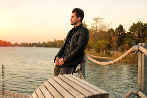 Handsome young man standing outside watching the sunset at the river