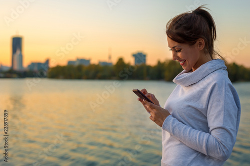 Beautiful young woman sending a text message on her smartphone outside
