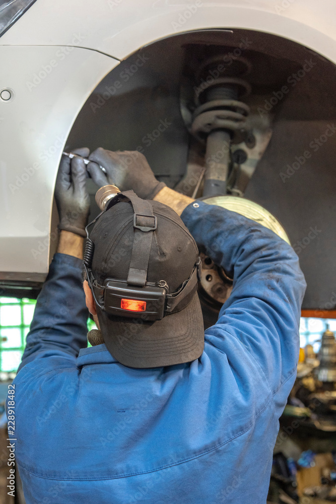 car mechanic worker repairing suspension of lifted automobile at auto repair garage shop station.