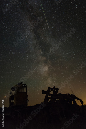 Old crawler tractor on the background of the milky way and flying meteor from the constellation Perseus