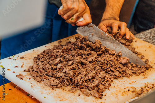 Close up of chef chopping up carne asada on a plastic cutting board with a blurry in motion chefs knife