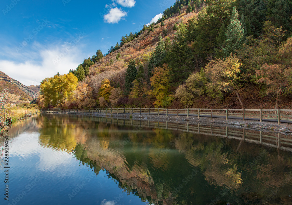 Lake lined by fence and fall foliage trees and hill