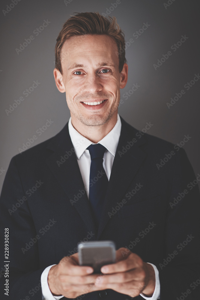 Smiling young business executive sending texts against a gray ba Smiling young business executive sending texts against a gray ba