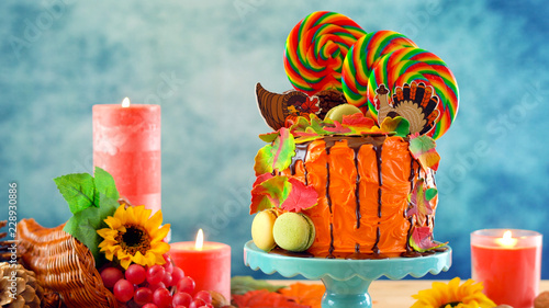 On trend Thanksgiving candyland novelty drip cake with colorful Fall leaves and cornucopia table setting.