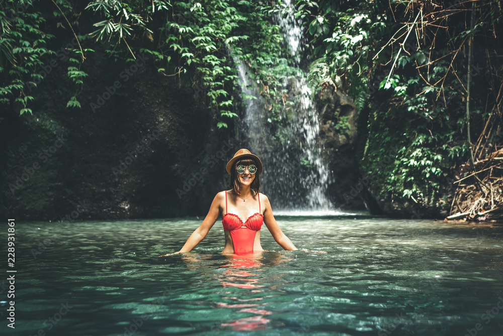Fototapeta premium Young woman tourist with straw hat in the deep jungle with waterfall. Real adventure concept. Bali island.