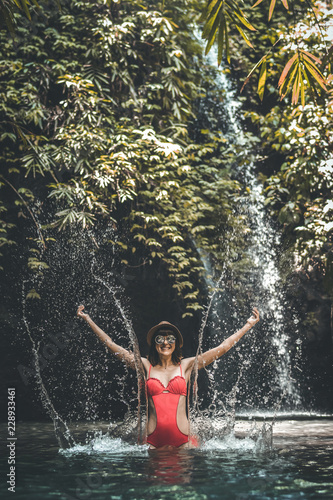 Happy Young woman tourist with straw hat in the deep jungle with waterfall. Real adventure concept. Bali island.