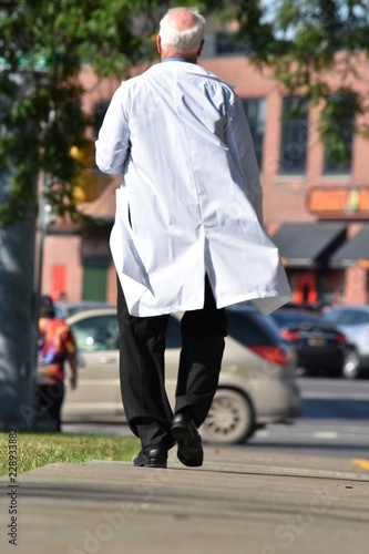 Senior Balding Male Doctor Walking On Sidewalk