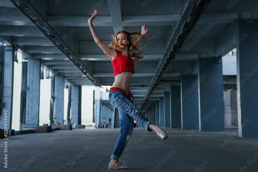 Fototapeta premium Ballerina dancing in jeans, t-shirt and pointe. Street performance. Modern art. Slender girl dancing on tiptoe.