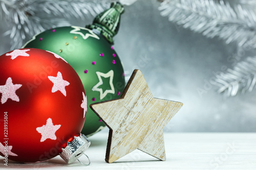 red and green christmas balls and wooden decorative star on blurred silver background with fir tree branches photo