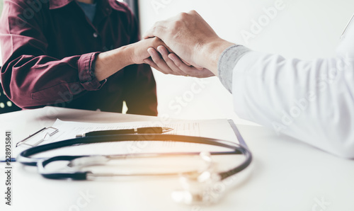 Doctor consoles the patient and holding hands with medical consultation at hospital.
