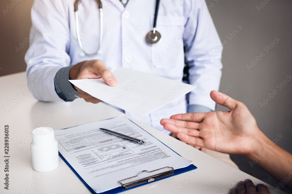 Asian male doctor talking in clinic room and handing a prescription to the patient. Asian male doctor talking in clinic room and handing a prescription to the patient.