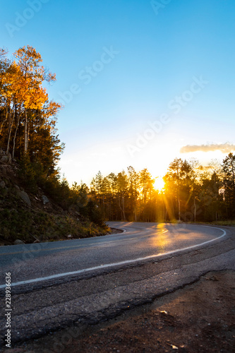 A road curving between the mountainside and trees on an autumn evening